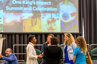 'Funmi speaking to a small group including Katharina, Nicole, and Anica, with student ambassador Chloe in a blue t-shirt nearby and Kawal seated to the left, in front of the One King's Impact Summit a