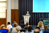 Nicole speaking at the podium to the seated audience during the summit, with a screen behind her displaying instructions.