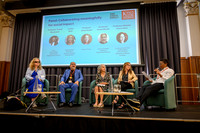 Five panellists seated on stage for 'Collaborating meaningfully for social impact': Anica, Kawal, Melanie, Lesley, and 'Funmi, who is speaking into a microphone as chair, with a guide dog resting besi