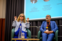 Anica speaking with hands raised while Kawal listens beside her on the panel, with the panellist line-up slide showing 'Expanding Safe Pathways to Sanctuary: Refugee Family Reunion' and 'Layers of Vis